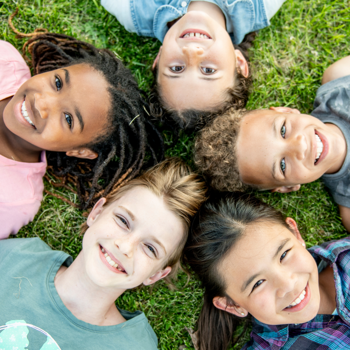 Five children lying on the grass with their heads together, smiling.